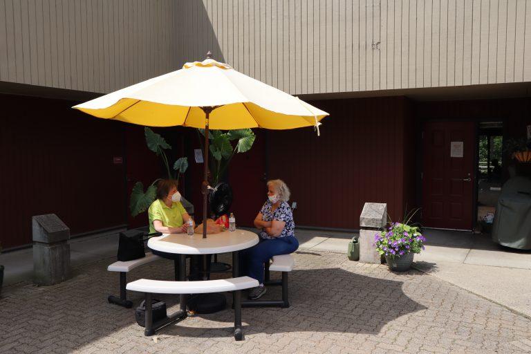 Photo of two individuals sitting outside on the patio at a table.