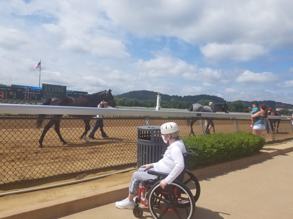 A person using a wheelchair is near a race track with horses.