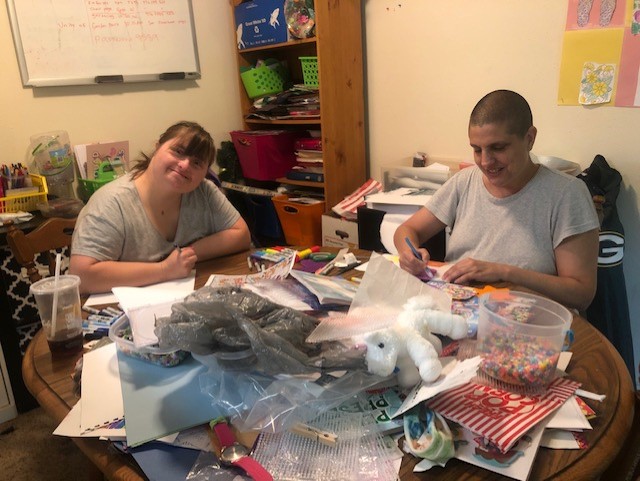 Beth and Susie sitting at a table, smiling and working on their pen pal projects.