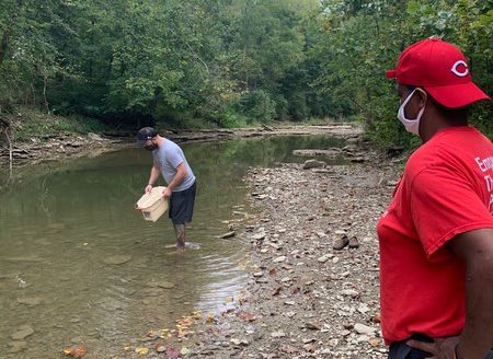 Photo of two men at a creek. One is in the creek looking for crawfish.