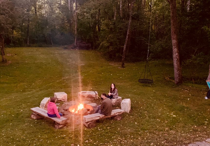 Photo of three people sitting, spaced out, around a fire outside.