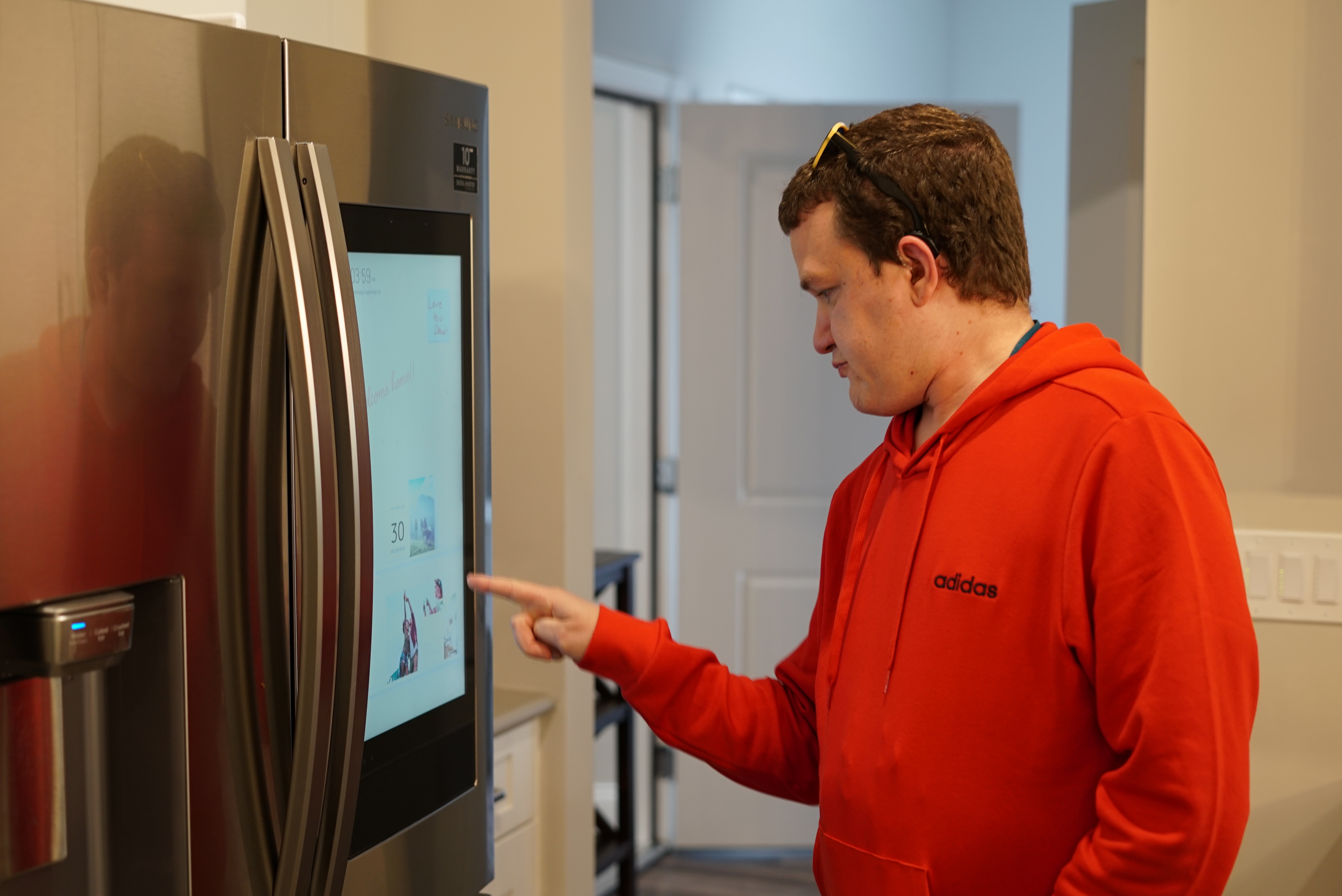 A man in a red hoodie touches a virtual screen on the smart refrigerator.
