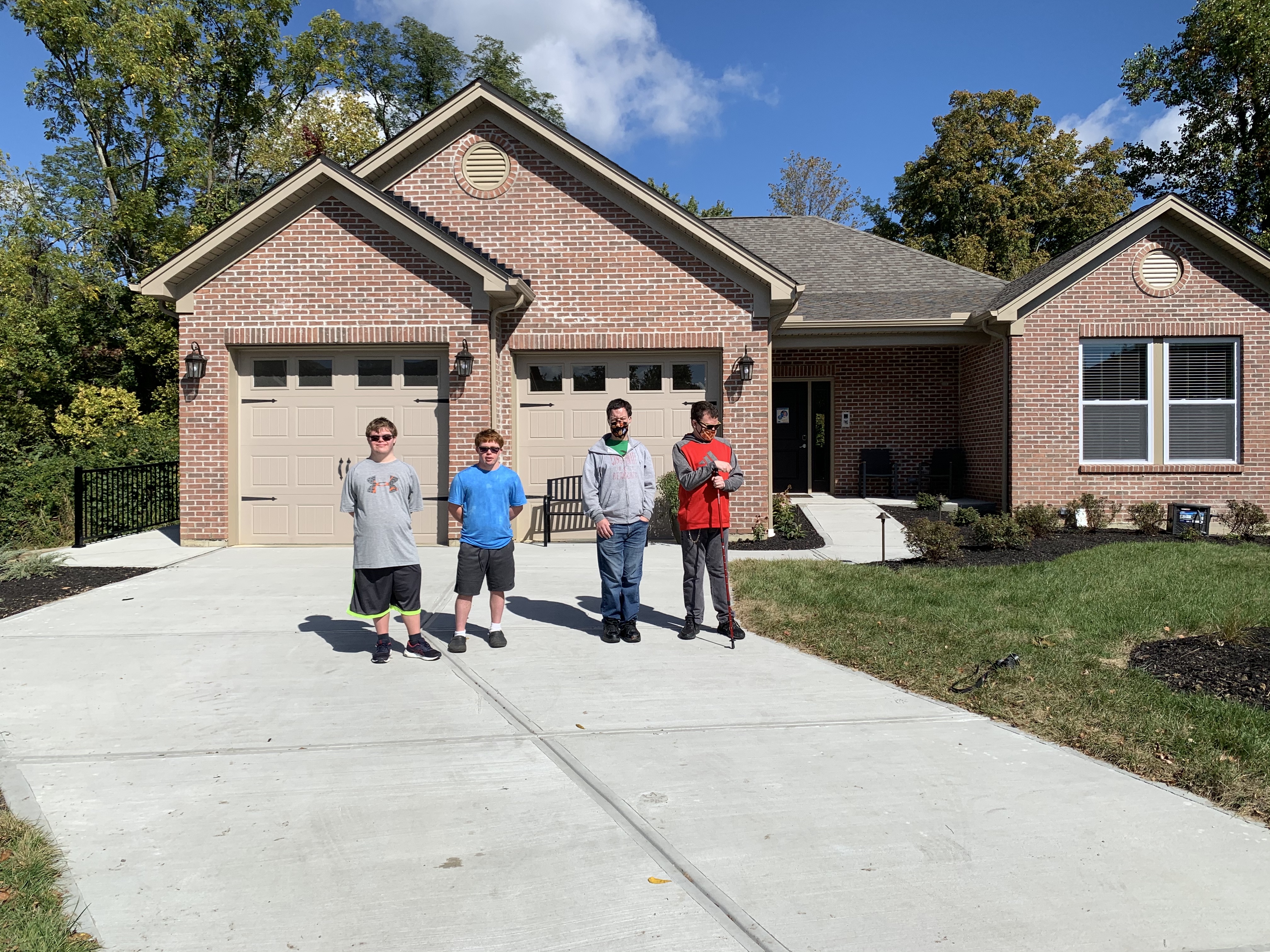 Four men, the residents of the Heidt Smart Living Home, stand in the driveway with the house behind them.