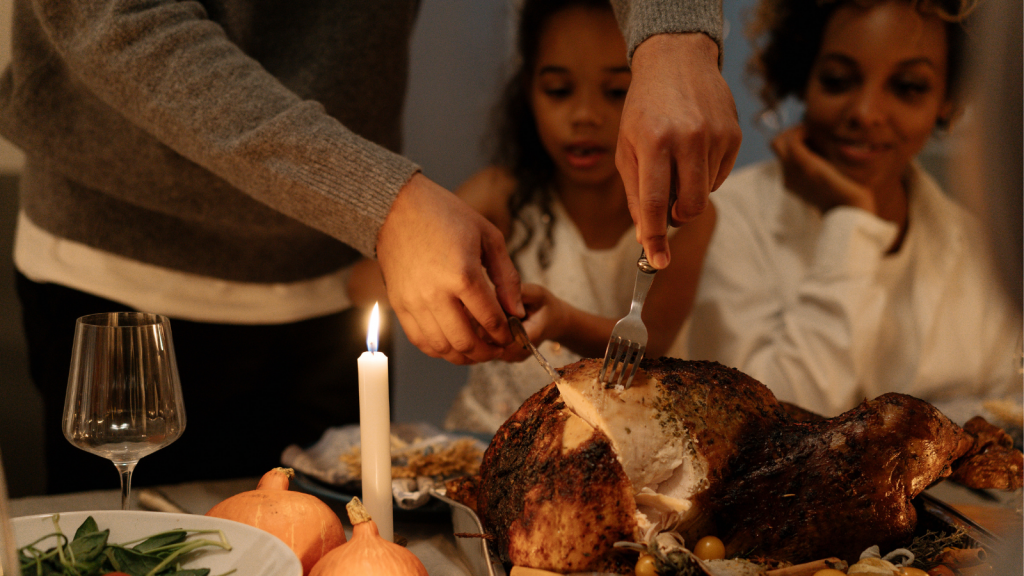 A cooked turkey is being cut into. A child and woman are in the background looking at the turkey.