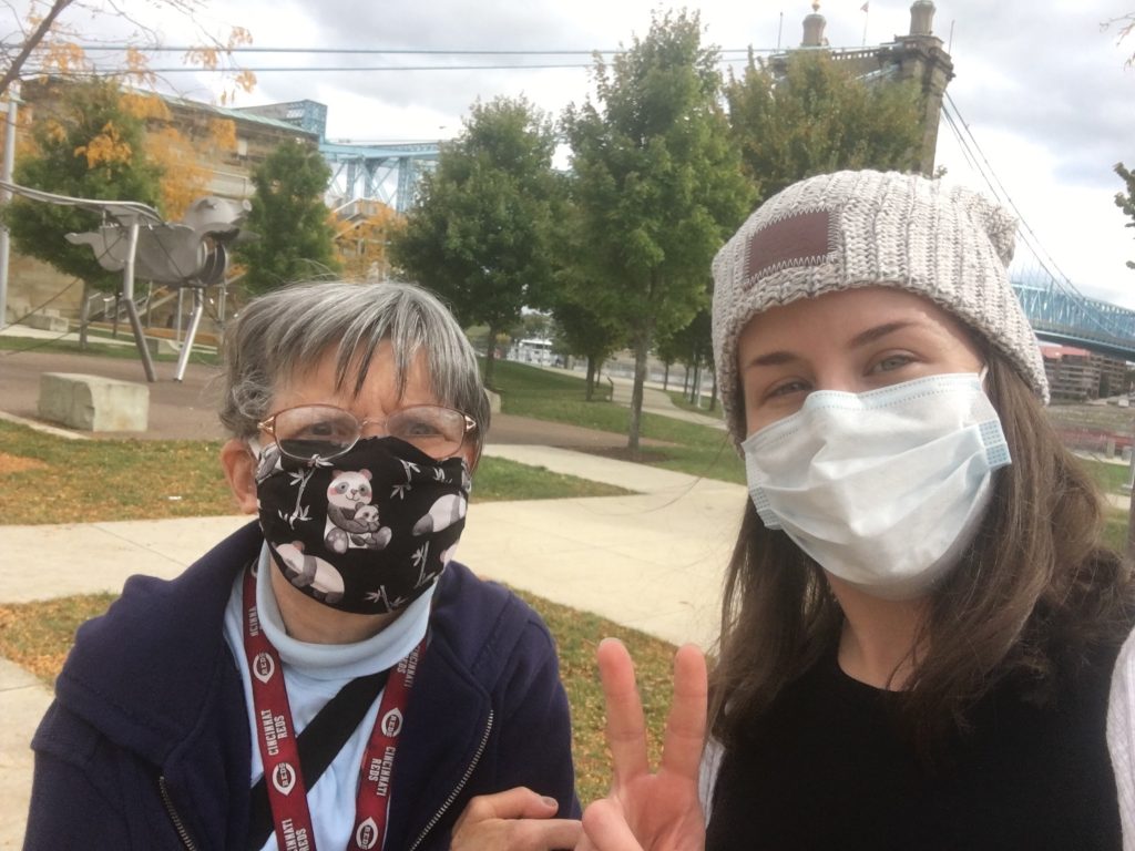 Image of two women wearing face masks. They are outside and one woman is holding up the peace sign with her fingers.