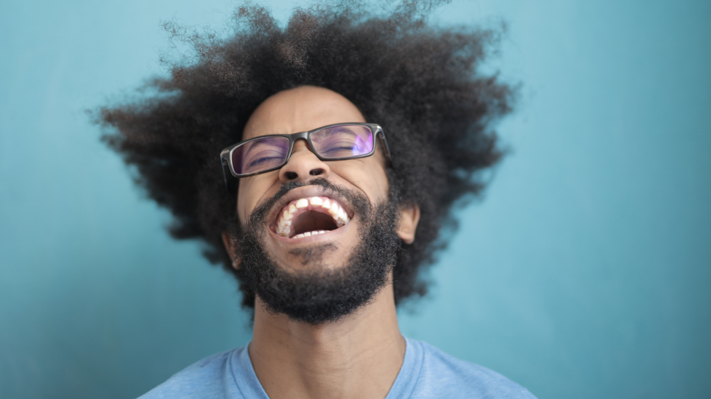 A man in front of a teal background is laughing.