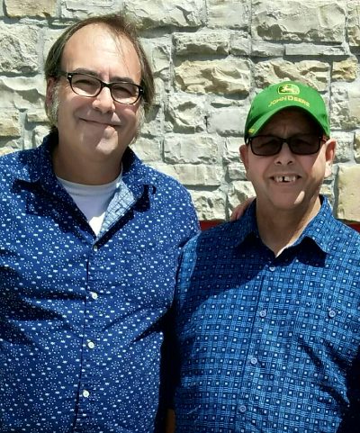 Photo of two men standing side by side outside and smiling.